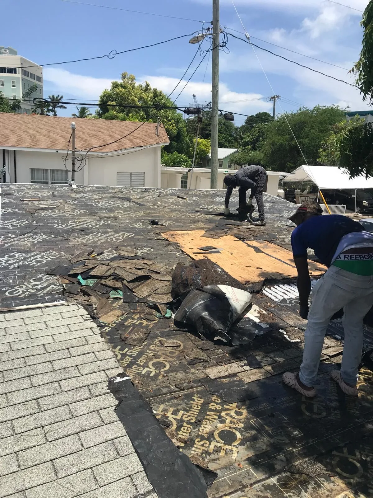 Two roofers removing damaged shingles from a Cayman home.